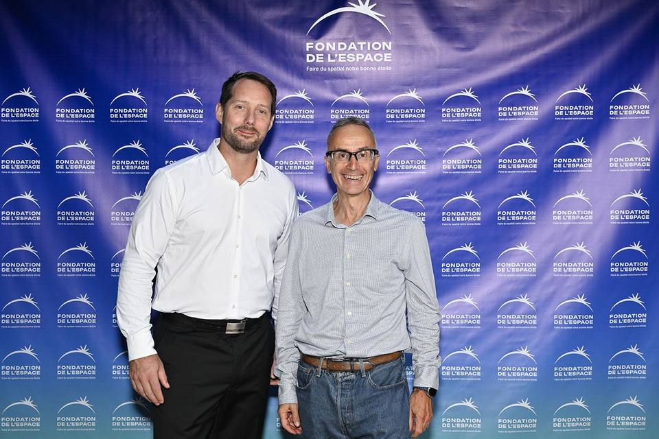 Deux convives souriant devant le mur aux logos de la Fondation