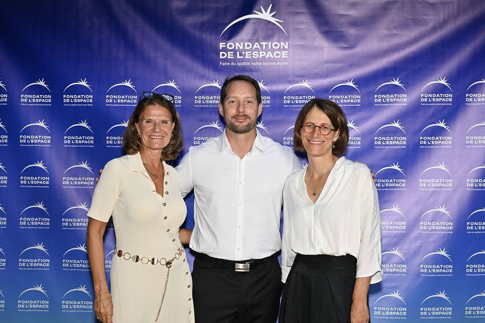 Trois convives souriant devant le mur aux logos de la Fondation