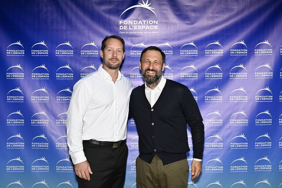Deux convives souriant devant le mur aux logos de la Fondation