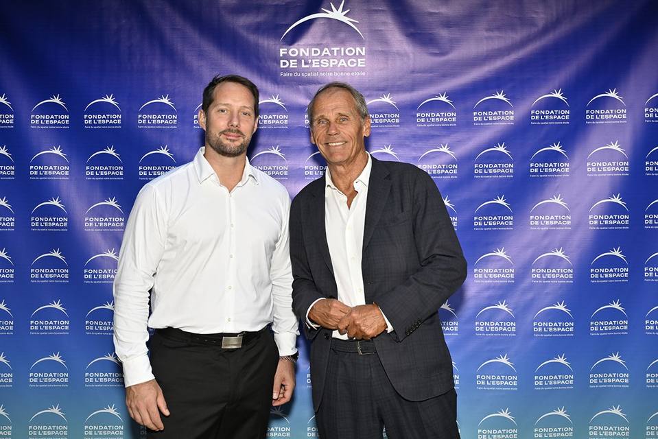 Deux convives souriants devant le mur aux logos de la Fondation