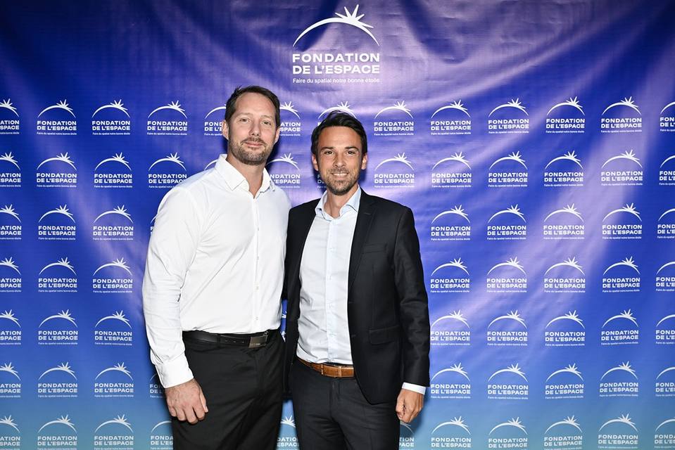 Deux convives souriant devant le mur aux logos de la Fondation