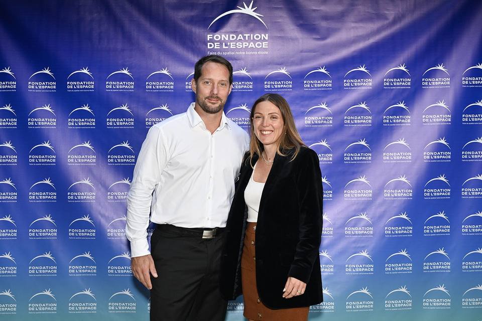 Deux convives souriant devant le mur aux logos de la Fondation