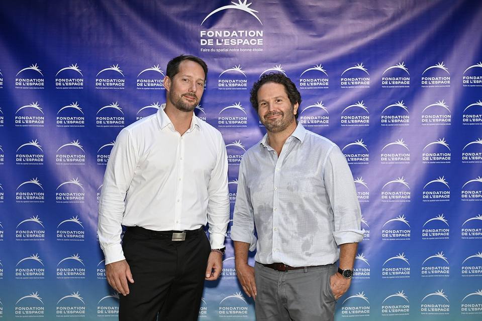Deux convives côte à côte devant le mur aux logos de la Fondation