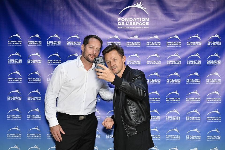 Deux convives prenant un autoportrait devant le mur aux logos de la Fondation