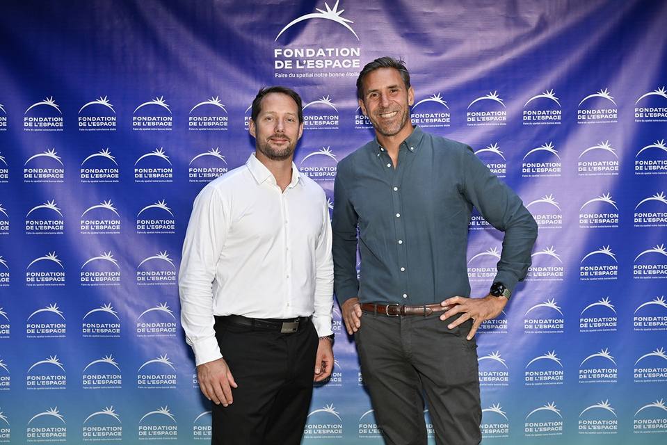 Deux convives souriants devant le mur aux logos de la Fondation