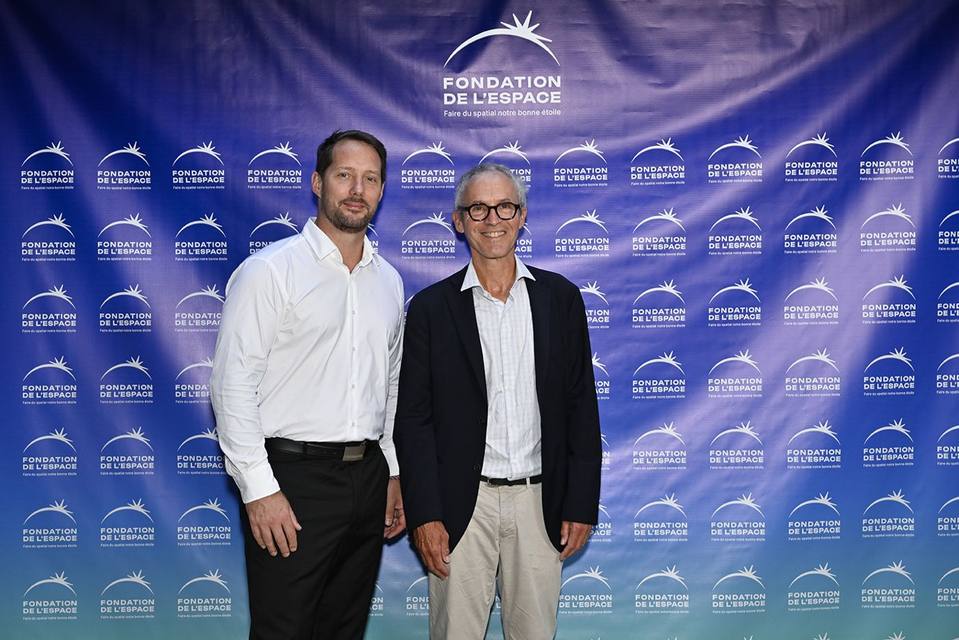 Deux convives, dont l'un à lunettes en veste sombre, devant le mur aux logos de la Fondation
