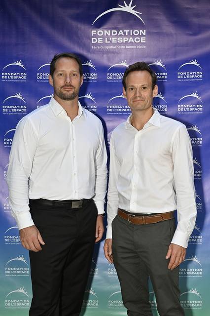 Portrait vertical de deux convives en chemise blanche devant le mur aux logos de la Fondation