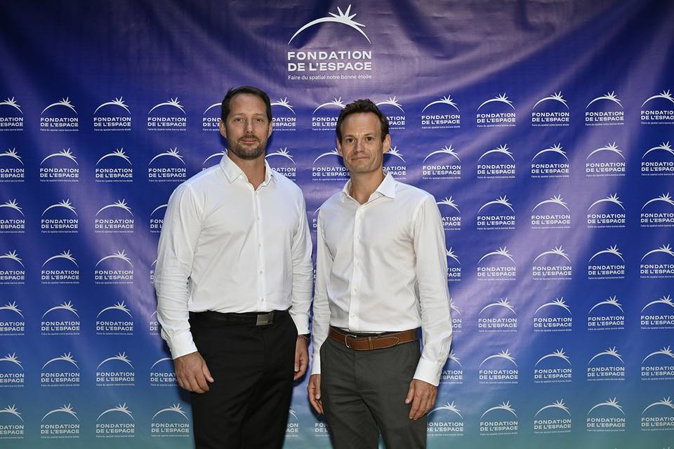 Deux convives en chemise blanche devant le mur aux logos de la Fondation