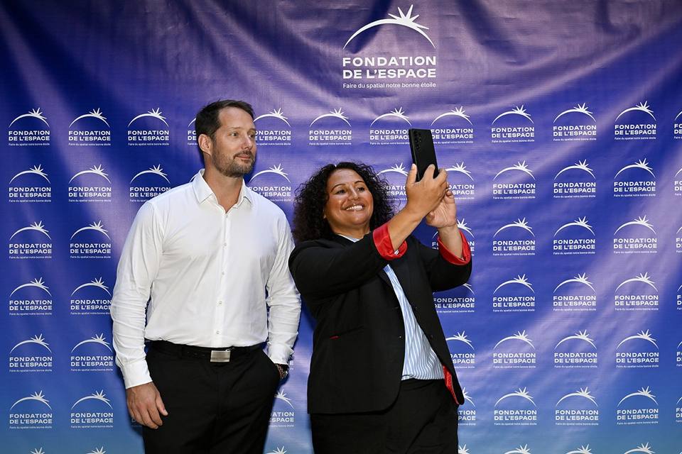 Une convive prenant un autoportrait avec un autre invité devant le mur aux logos de la Fondation
