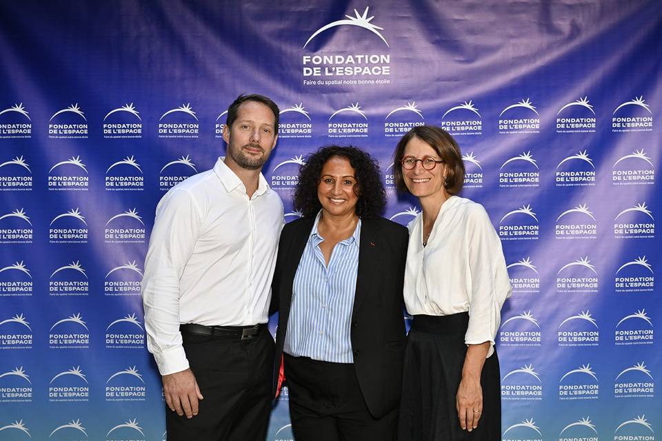 Trois convives souriants devant le mur aux logos de la Fondation