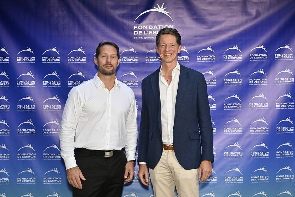 Deux convives, dont l'un en veste bleue, devant le mur aux logos de la Fondation