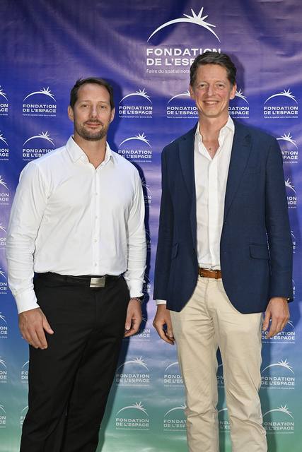 Portrait vertical de deux convives, dont l'un en veste bleue, devant le mur aux logos de la Fondation