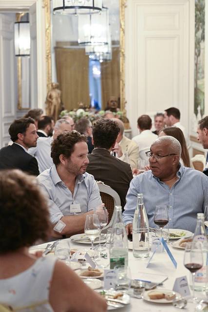 Deux convives en conversation à table, salle dressée en arrière-plan