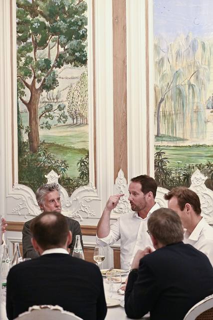 Convive en chemise blanche s'exprimant à table devant les peintures murales