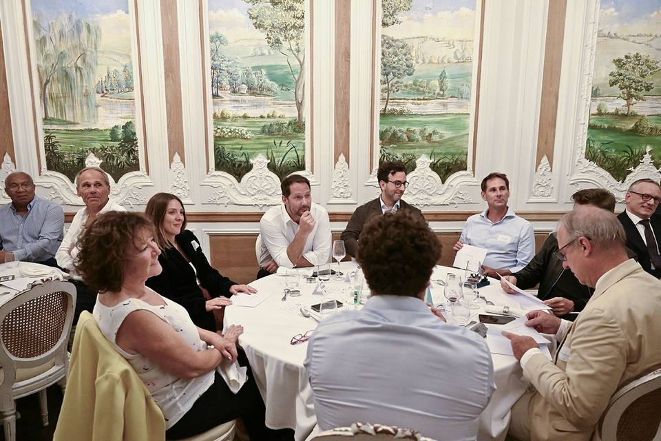 Convives réunis autour d'une table ronde devant les panneaux peints du salon