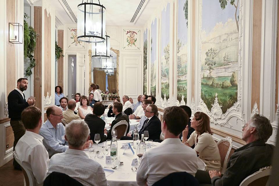 Vue d'ensemble du dîner, intervenant debout à gauche et convives attentifs