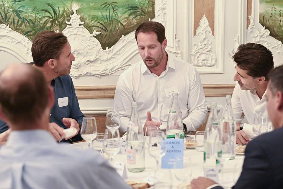 Convives échangeant à table devant les panneaux peints du salon