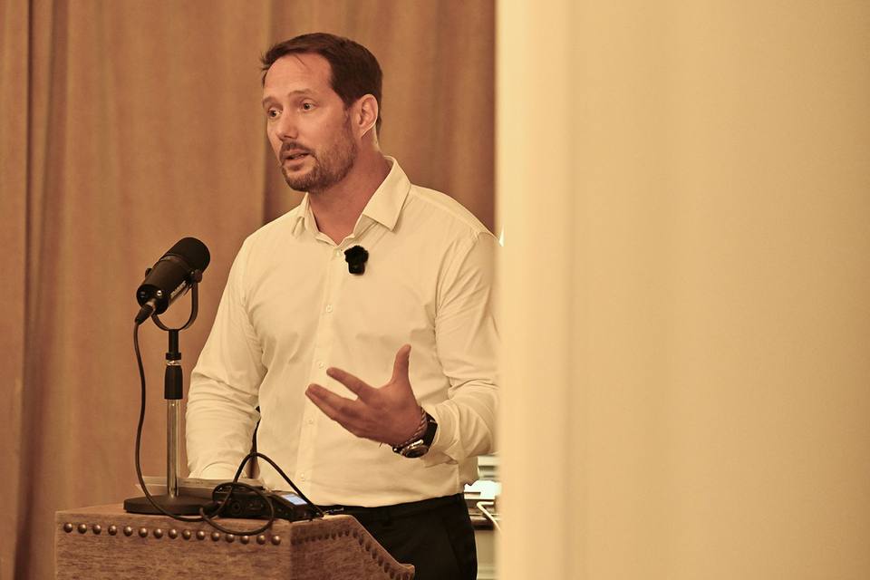 Intervenant en chemise blanche prenant la parole au microphone